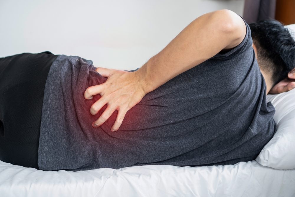 A man lying down and clutching his lower back in pain