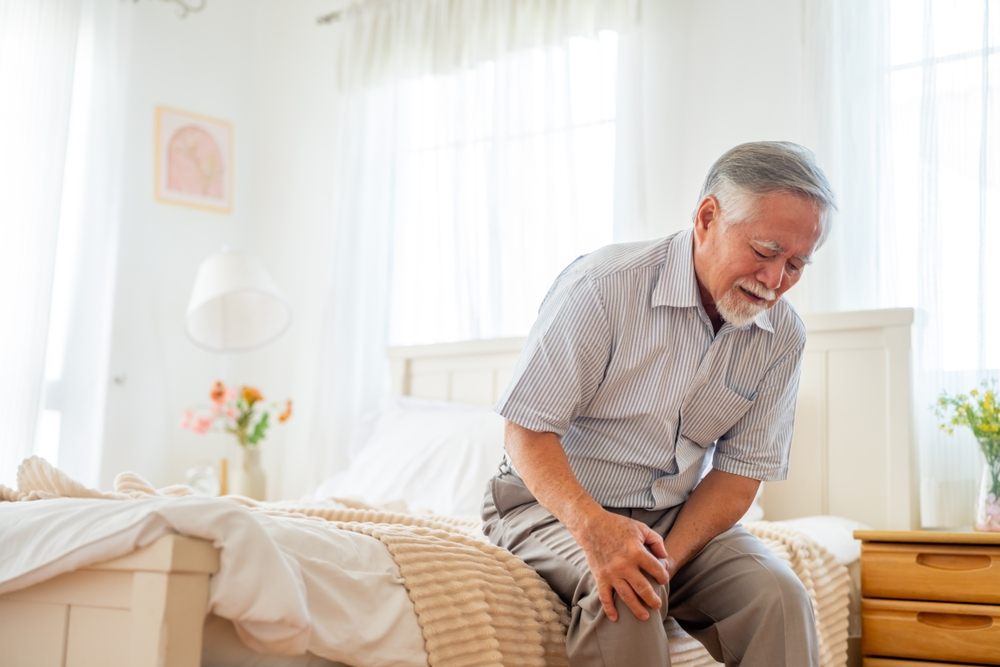 An older adult sitting on a bed, experiencing persistent pain at home